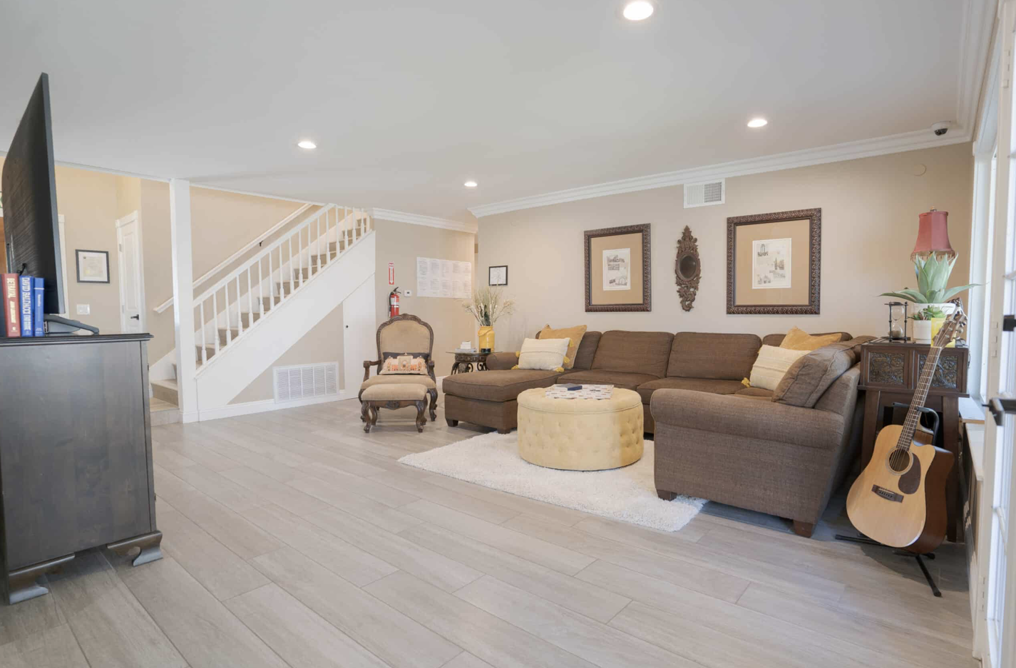 Lounge with couch, a TV, and a guitar, with a stairwell in view.