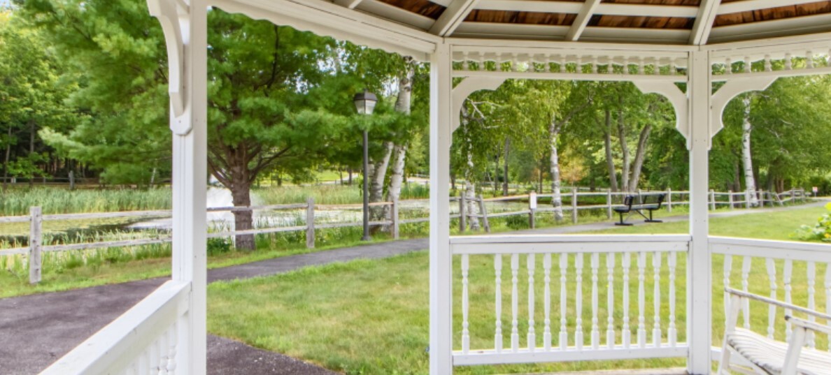 Gazebo overlooking a path, greenery, and a wooden fence.