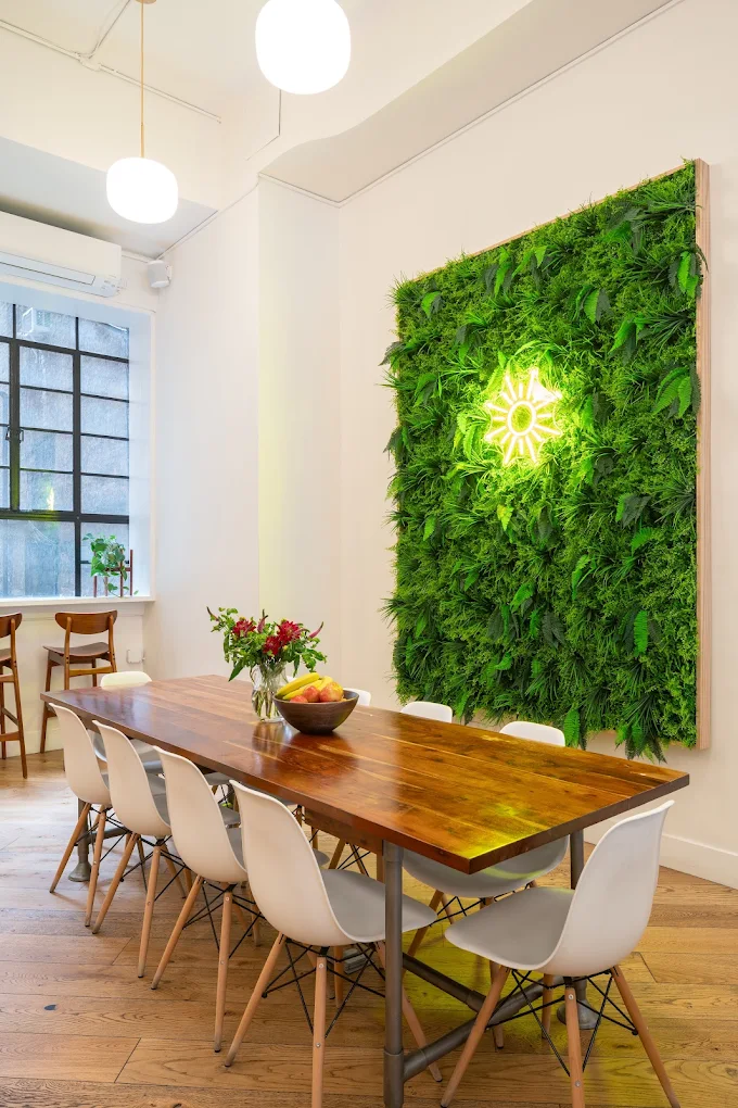 Dining table beside a green plant wall and large windows