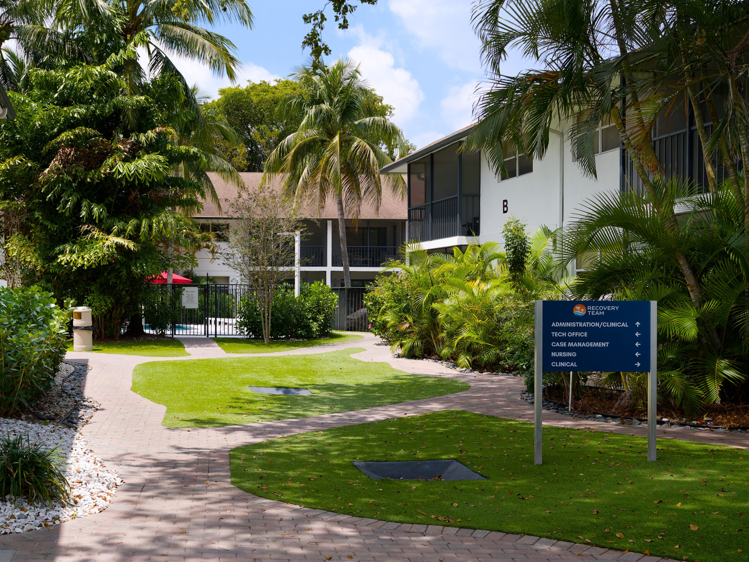Walkway through landscaped campus with palm trees and buildings.