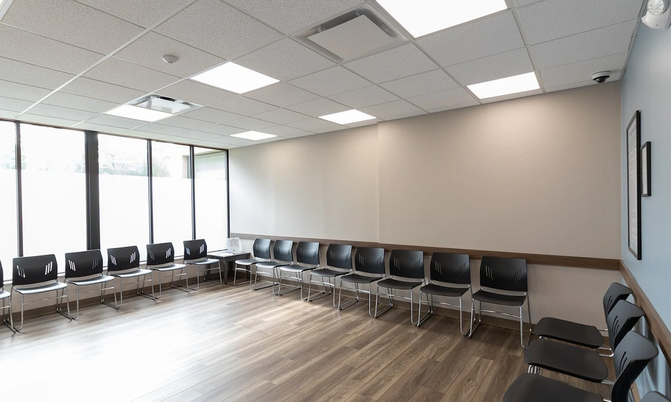Spacious BrightView Health waiting room with black chairs arranged along the walls, large windows, wood-look flooring, and bright overhead lighting