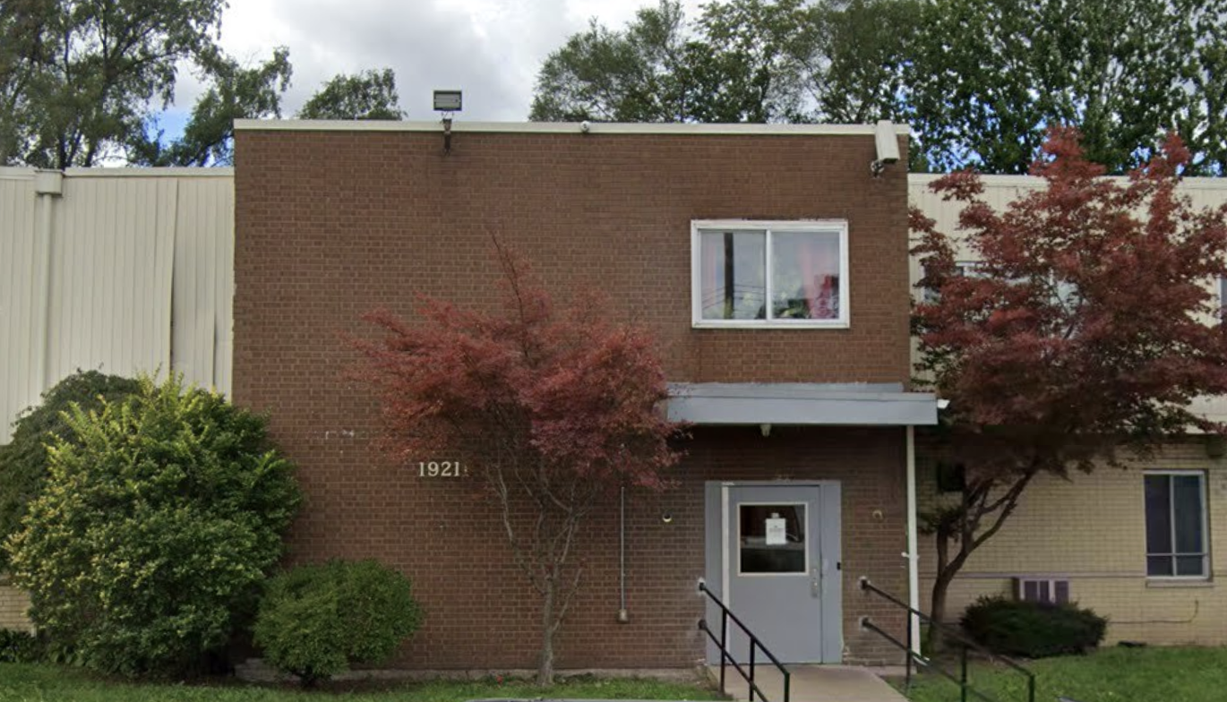 Red brick building with gray entrance door and landscaped trees