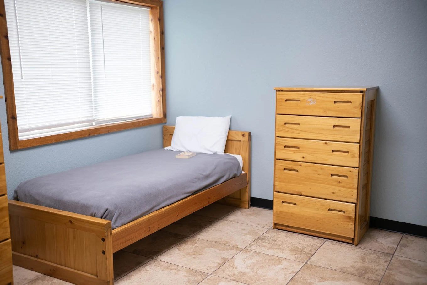 Single bed with wood dresser in a tiled rehab bedroom