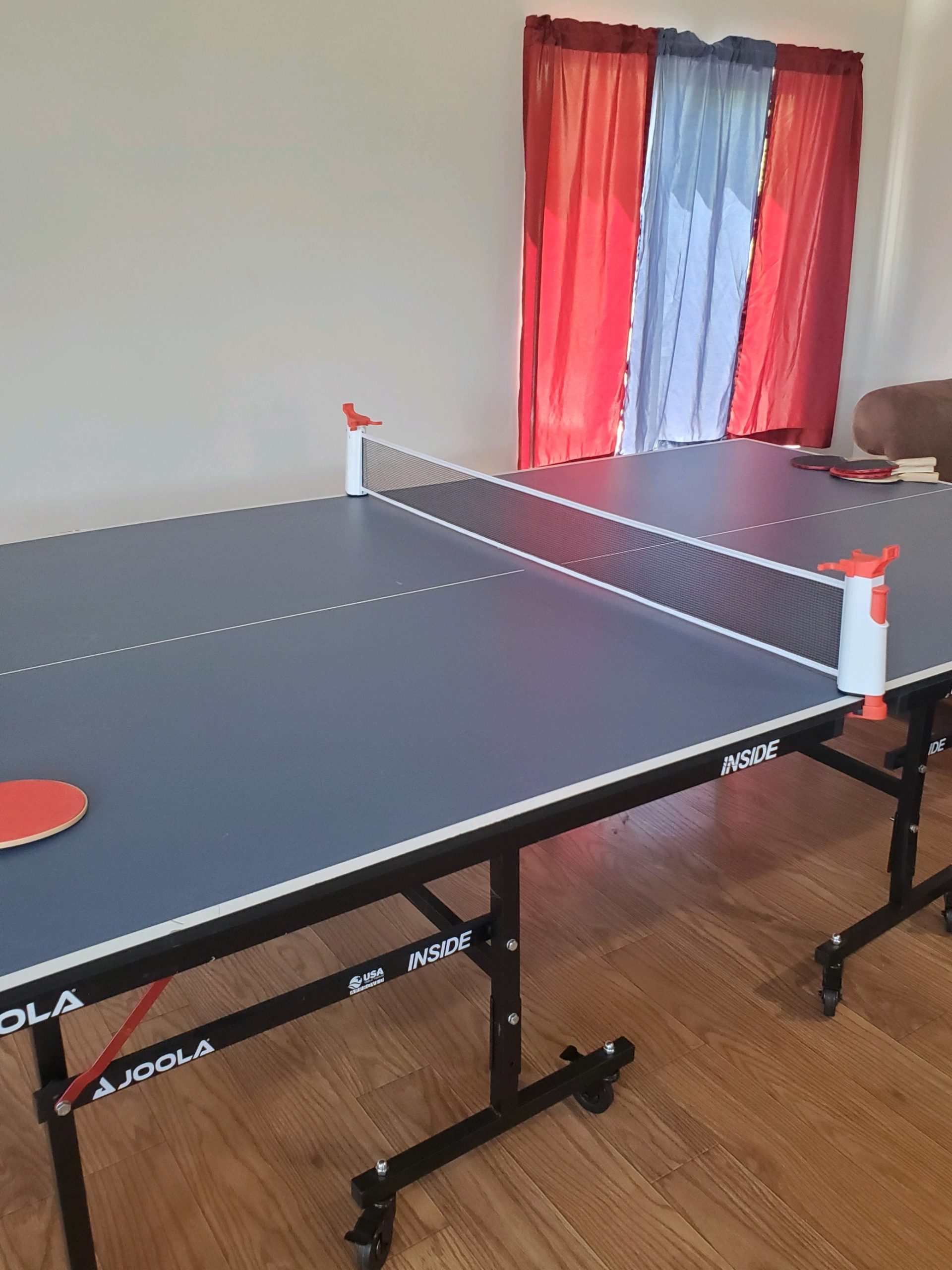 JOOLA table tennis setup with paddles in a room with red and blue curtains, offering indoor recreational space