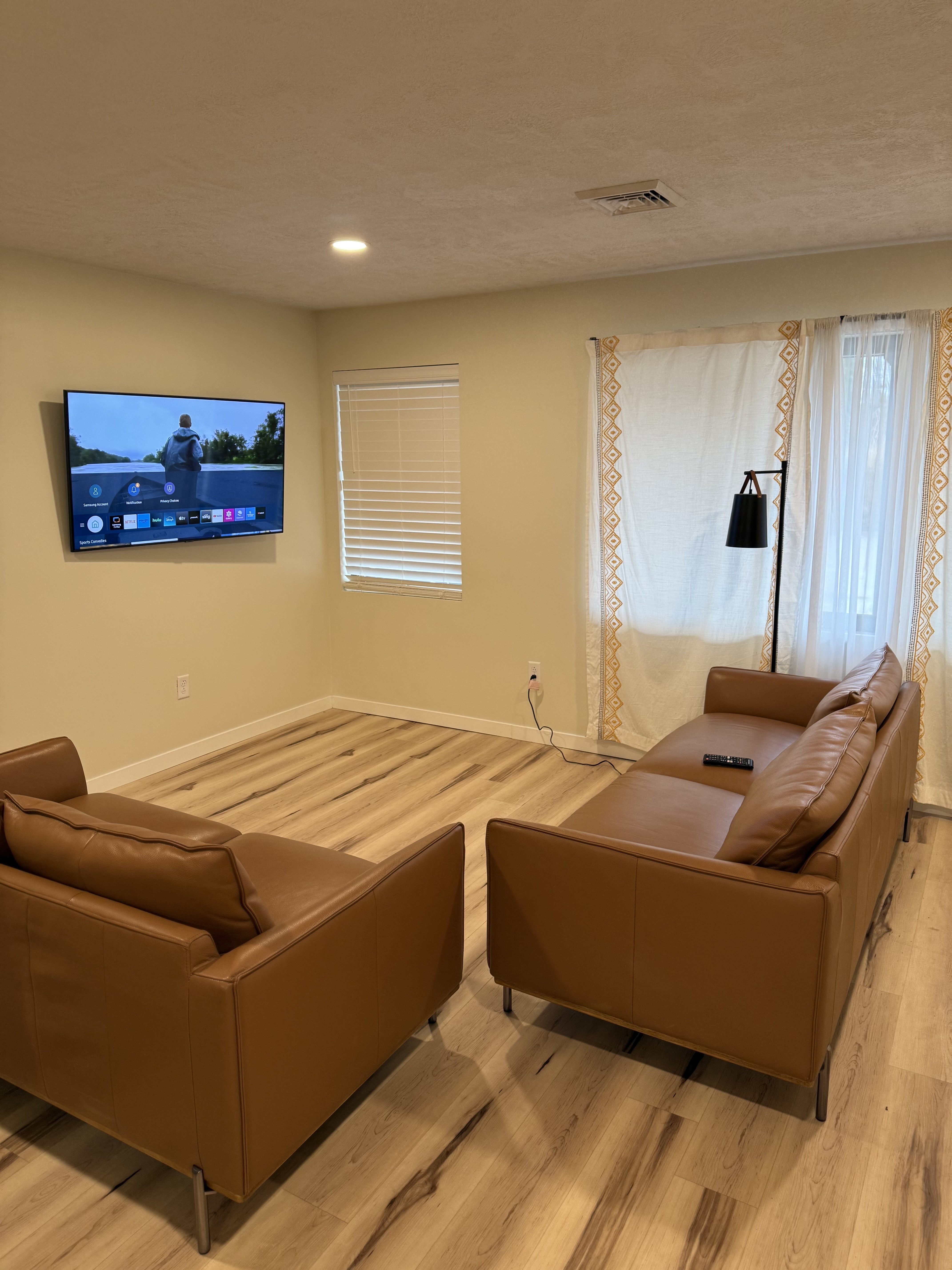Living room with wall-mounted TV, leather sofa, and floor lamp.