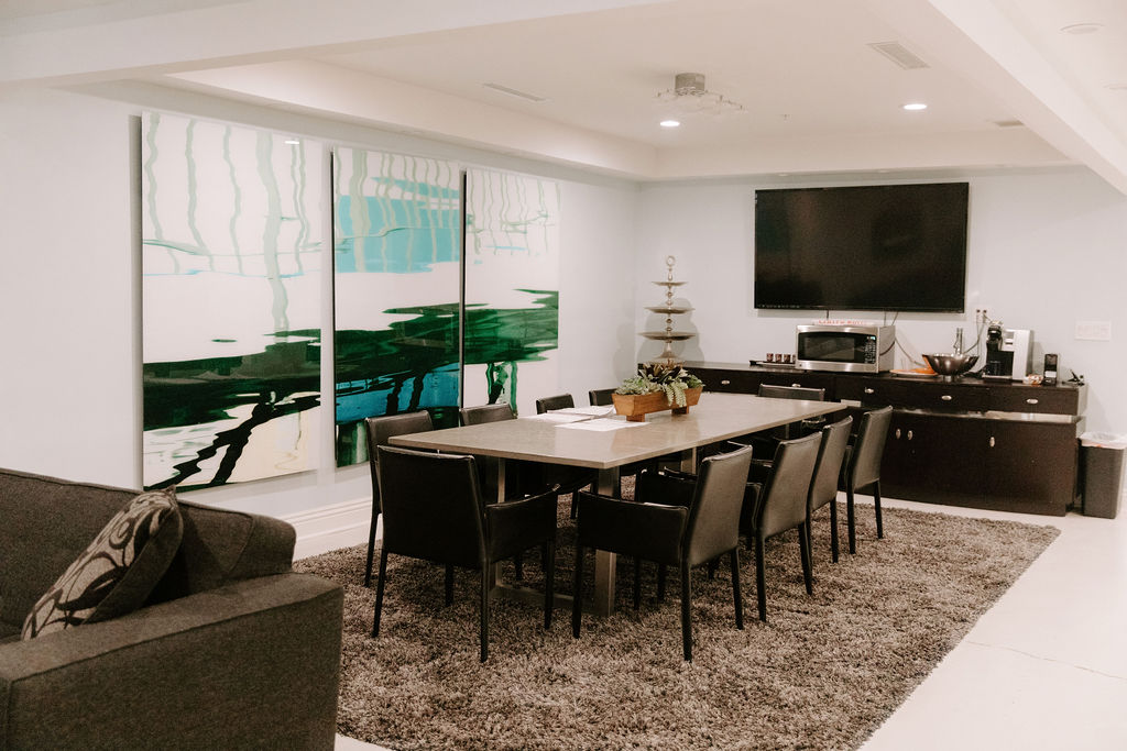 Elegant dining room with round glass-top table, decorative chairs, ornate chandelier, and a black floral area rug
