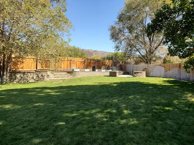Spacious fenced yard with trees, grass, and seating areas