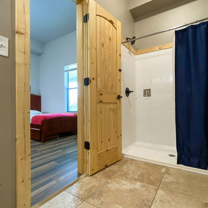 Shared bathroom with shower and wooden door to bedroom