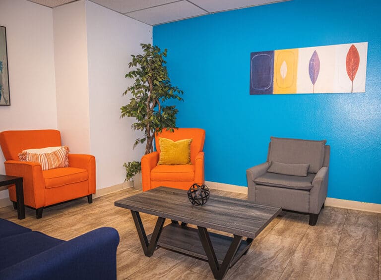 A lounge area with orange chairs, a gray armchair, and a blue accent wall.