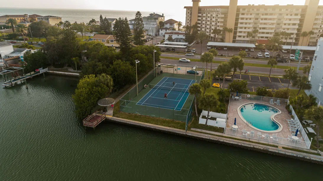 Aerial view of facility showing a tennis court, pool, and greenery.