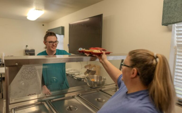 Staff hands food tray to resident at cafeteria counter