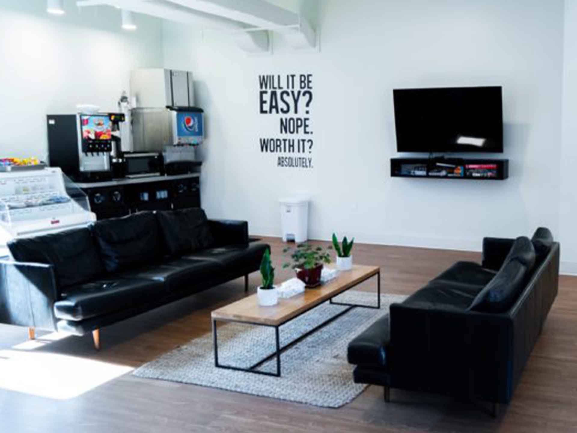 A lounge with black couches, a TV, and a snack bar