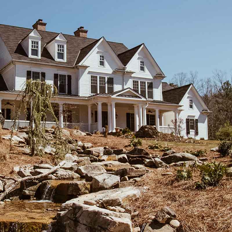 Large white estate-style building with wraparound porch and landscaped grounds
