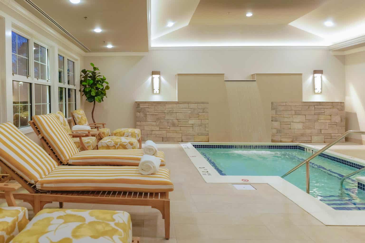 Indoor pool with striped lounge chairs and waterfall wall