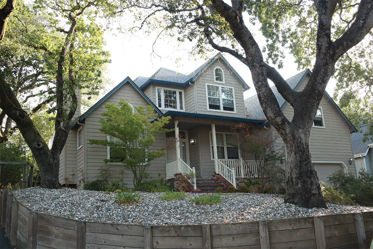 Two-story tan house with porch and large front trees