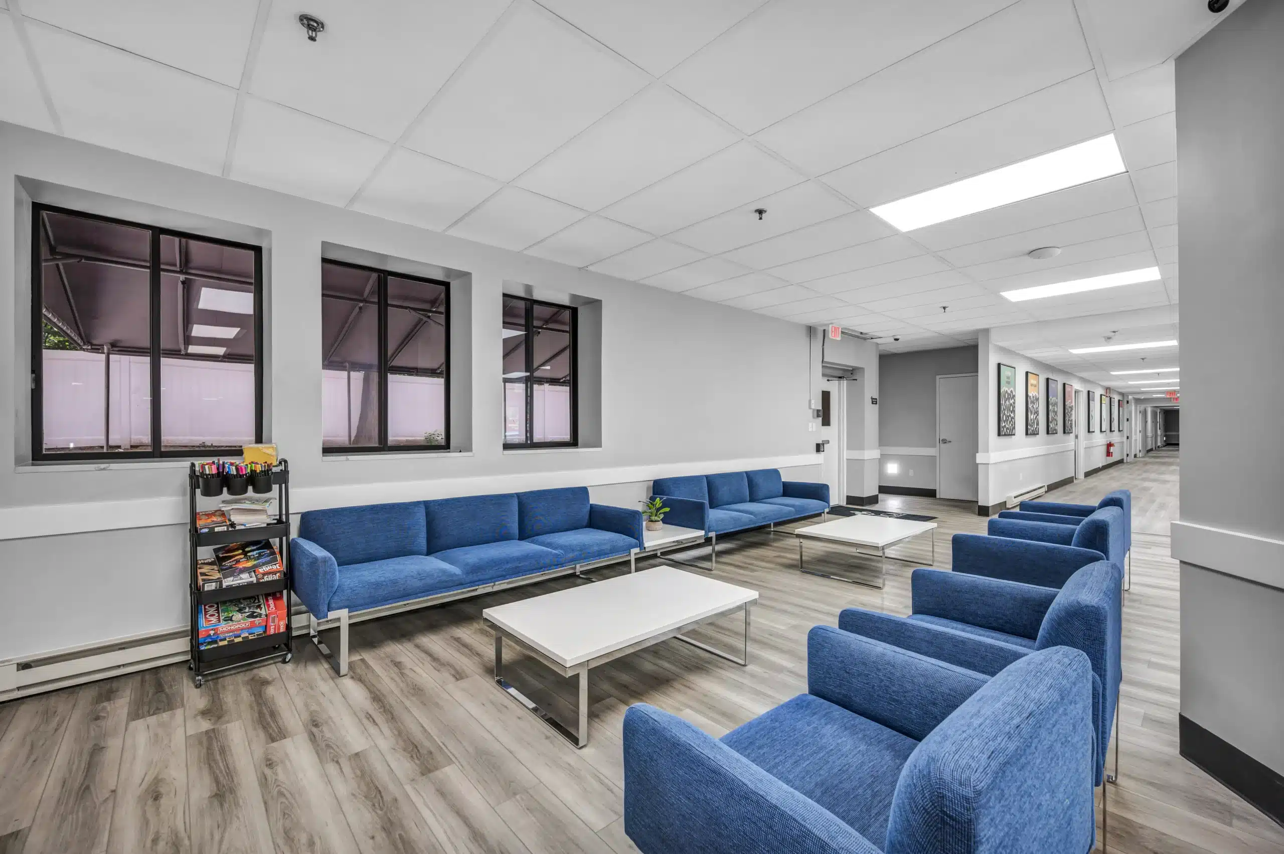 Indoor lounge with blue sofas, armchairs, white tables, and board games at Boca Recovery Center Massachusetts