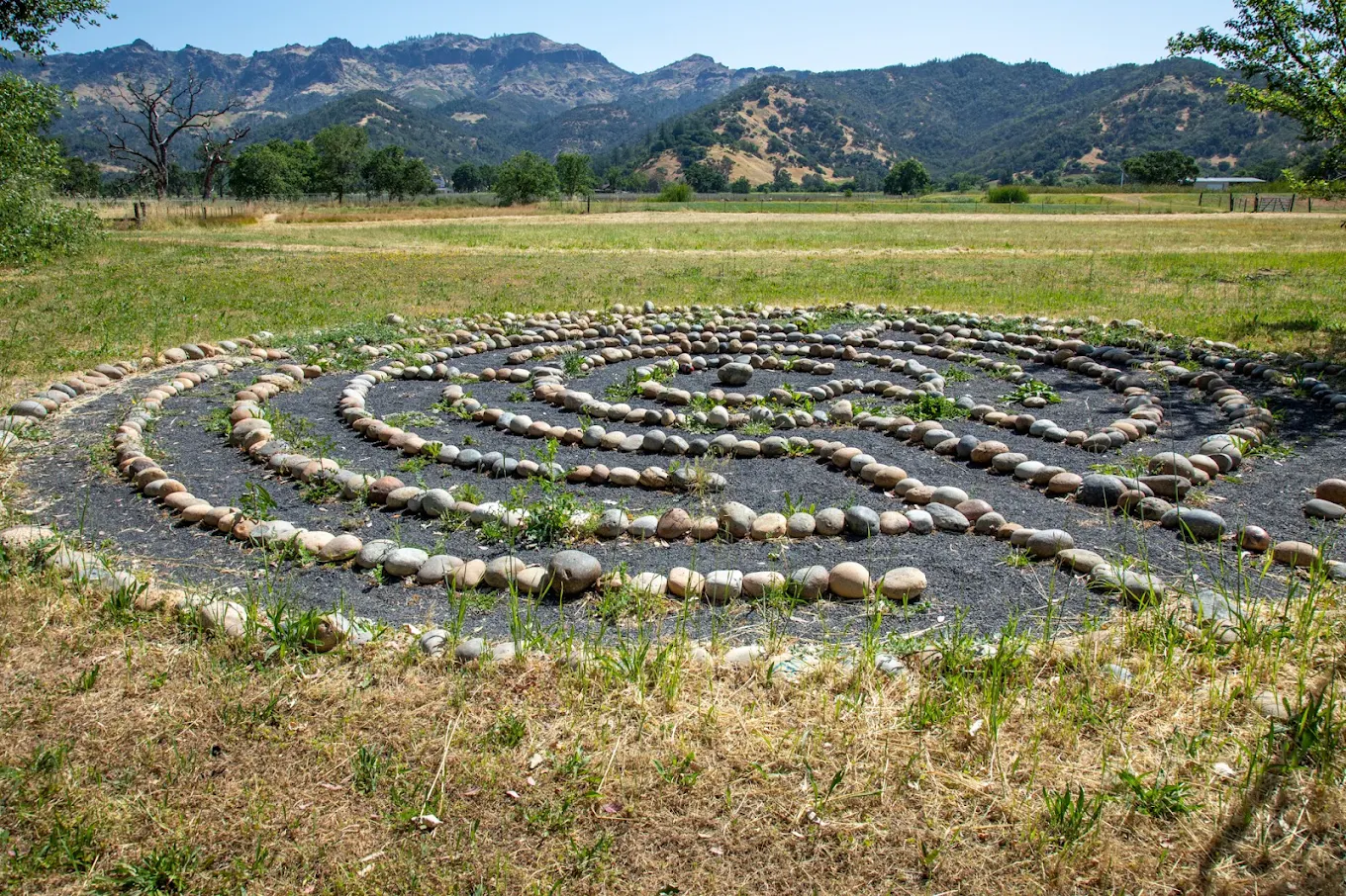 Stone labyrinth in a grassy field with mountain backdrop
