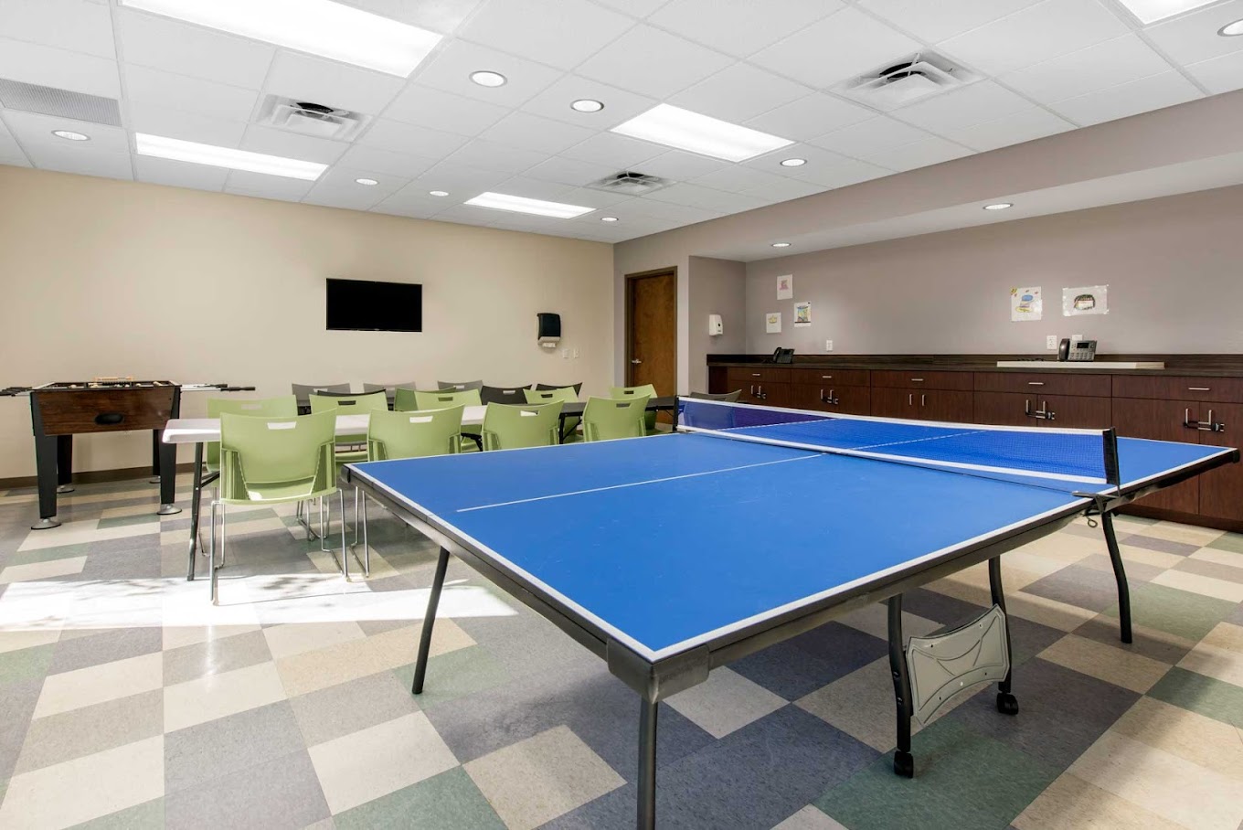 A recreational room featuring a ping-pong table, foosball, and seating.