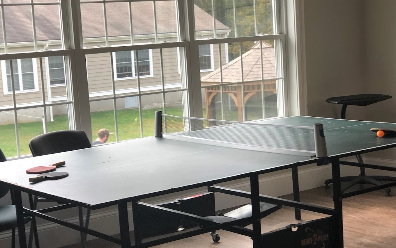 A recreation room with a ping pong table and large windows.