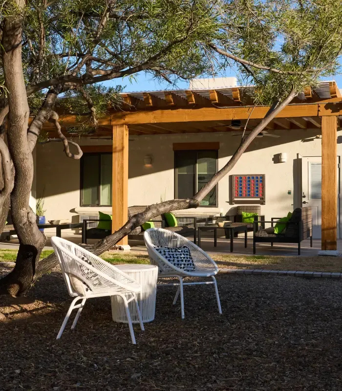 Patio seating under pergola beside a tree and garden area.
