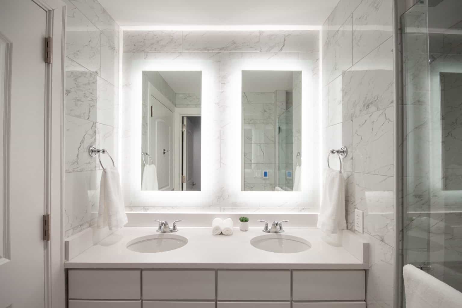 Double vanity bathroom with backlit mirrors and marble tile
