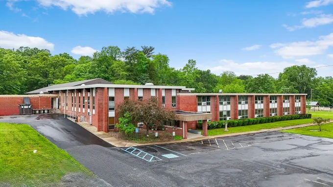 Large brick treatment facility with multiple wings, parking area, and surrounding trees.
