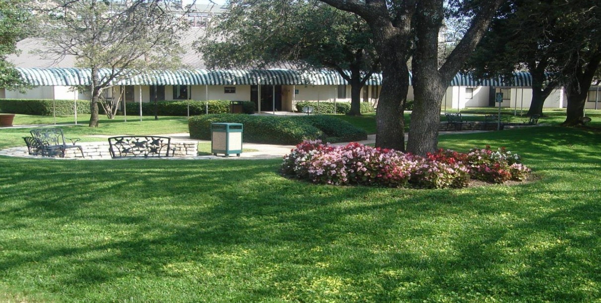 Landscaped outdoor courtyard with walking paths, benches, mature trees, and garden seating for relaxation