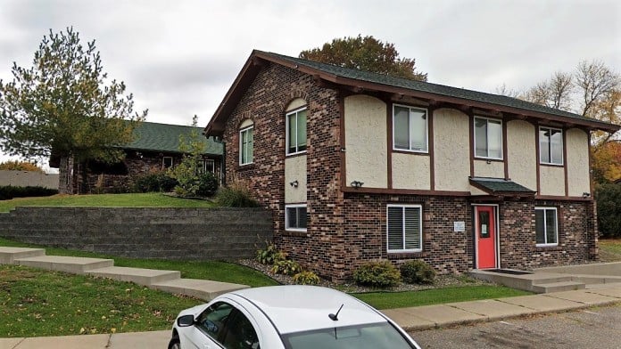  Two-story brick building with red door and small lawn out front