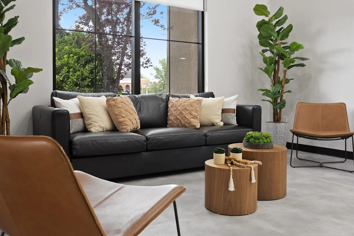 Cozy lounge with black leather couch, brown chairs, and large windows