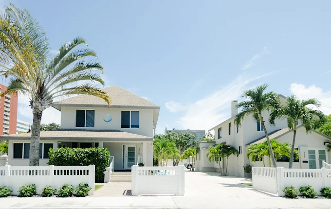 White rehab facility exterior with palm trees and fencing