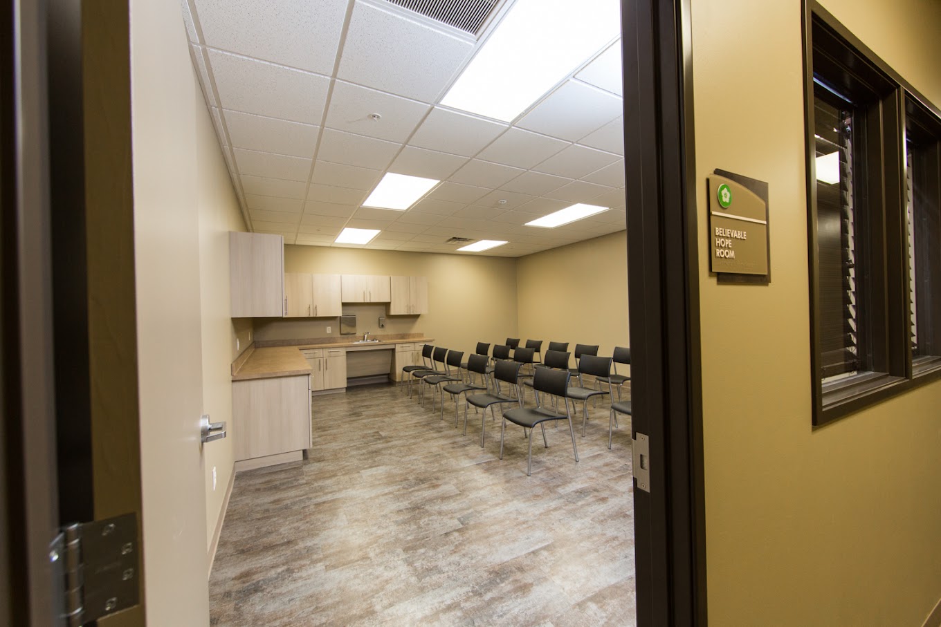 Group therapy room with rows of black chairs and kitchenette in the background