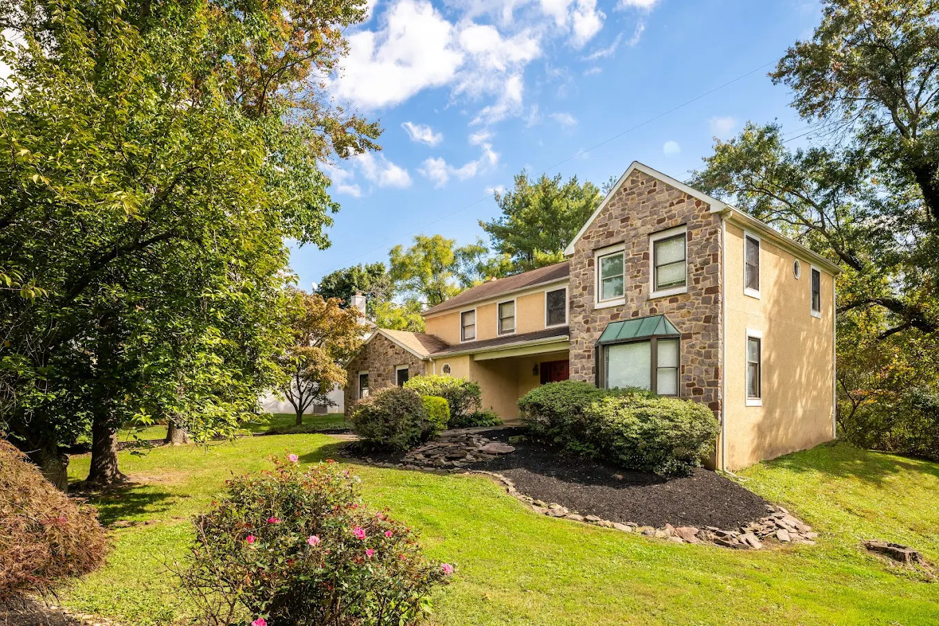 Stone and stucco home with trees and front lawn