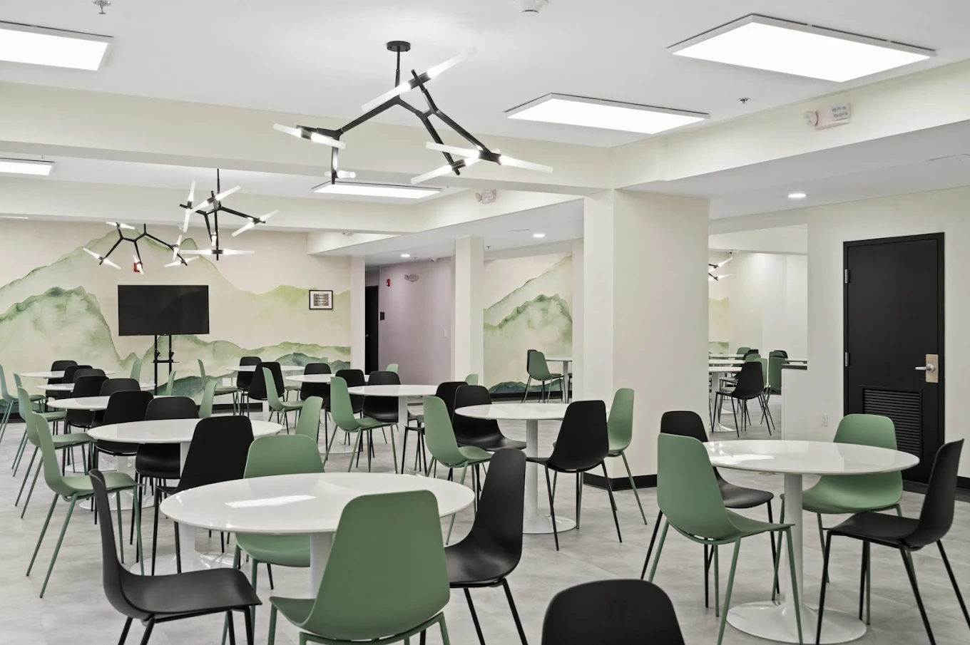 Contemporary cafeteria with round tables, green and black chairs, and mural wall