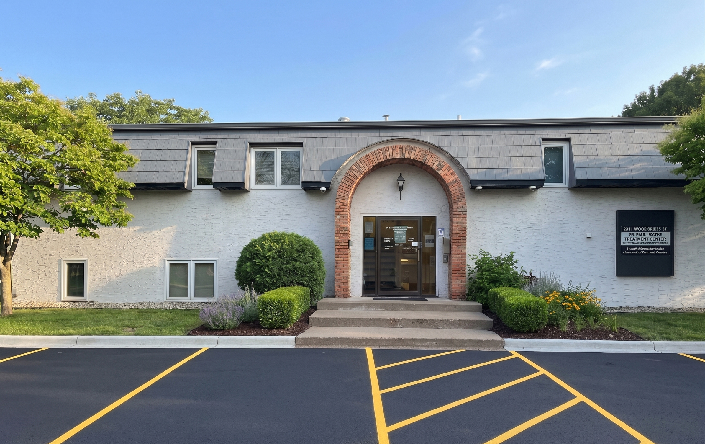 Brick arch entry of a rehab facility with trees and parking
