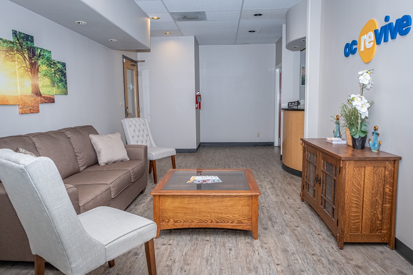 Lounge with a brown couch, white chairs, and wooden furniture.