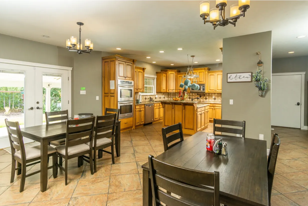 Warm wood-tone kitchen with hanging lights, central island, and multiple dining tables with dark chairs