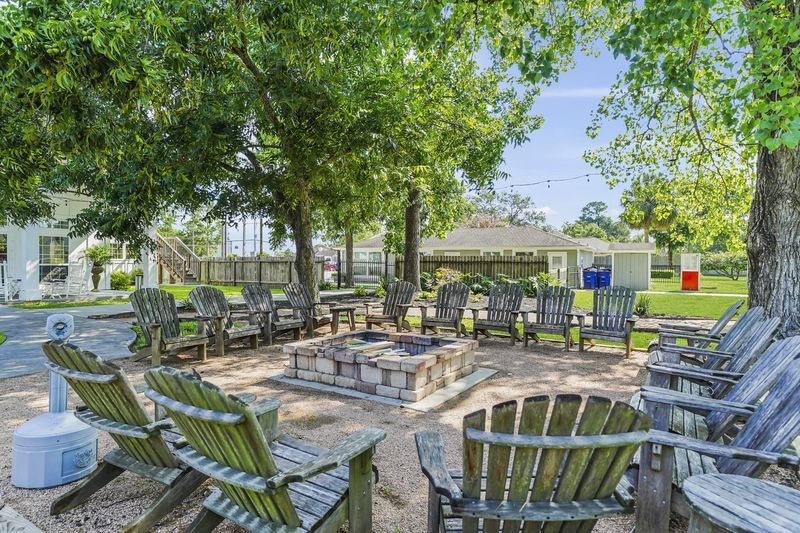 Circular fire pit surrounded by wooden chairs under tree canopy in grassy backyard