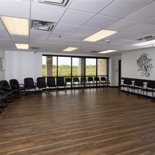 Spacious group therapy room with chairs arranged along the walls and a large window view of greenery
