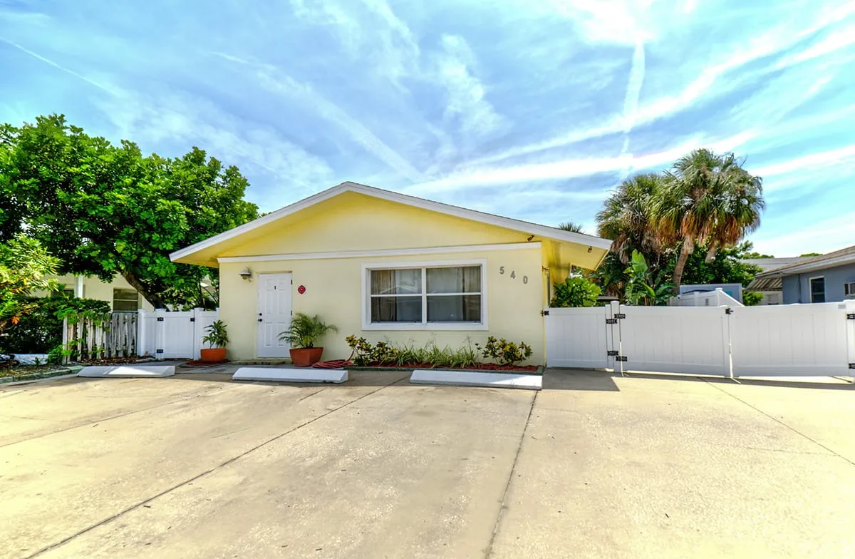 Yellow single-story home with white fencing and potted plants