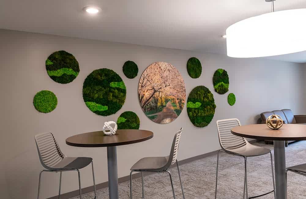 A dining area with round tables and a wall decorated with green art.