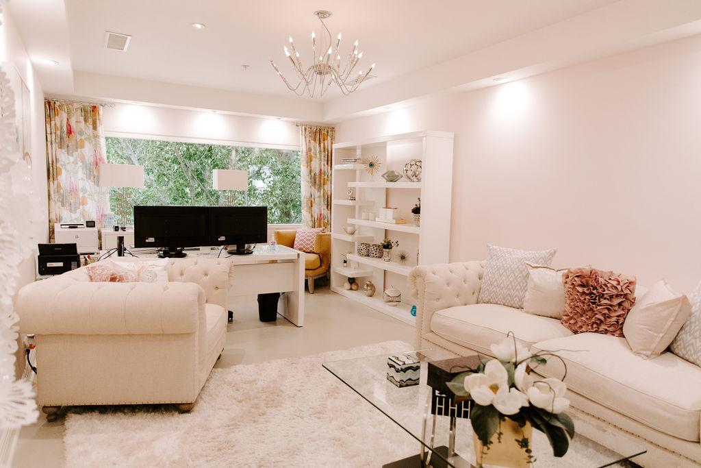 Comfortable living space with tufted sofas, white shag rug, bookshelves, and dual-monitor workspace near a large window