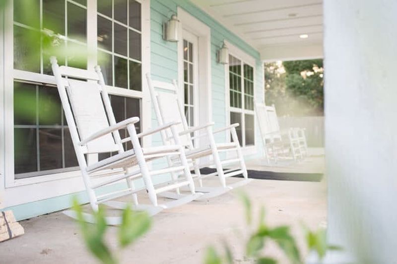 Light blue building with white rocking chairs on a shaded front porch