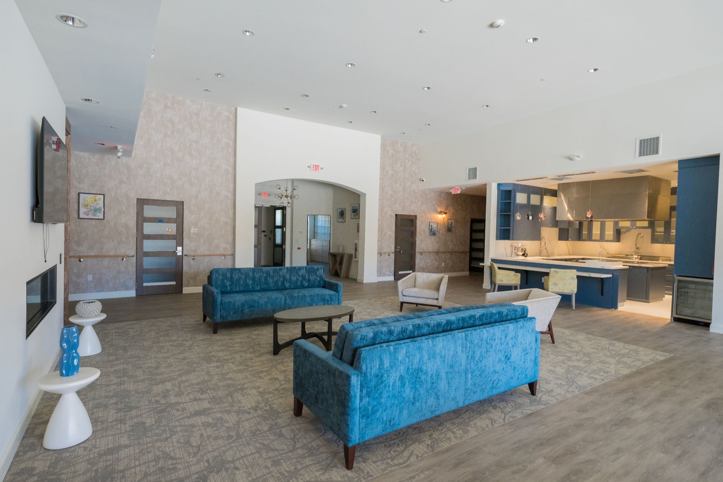 Lounge with blue couches, a modern kitchen, and bright lighting.