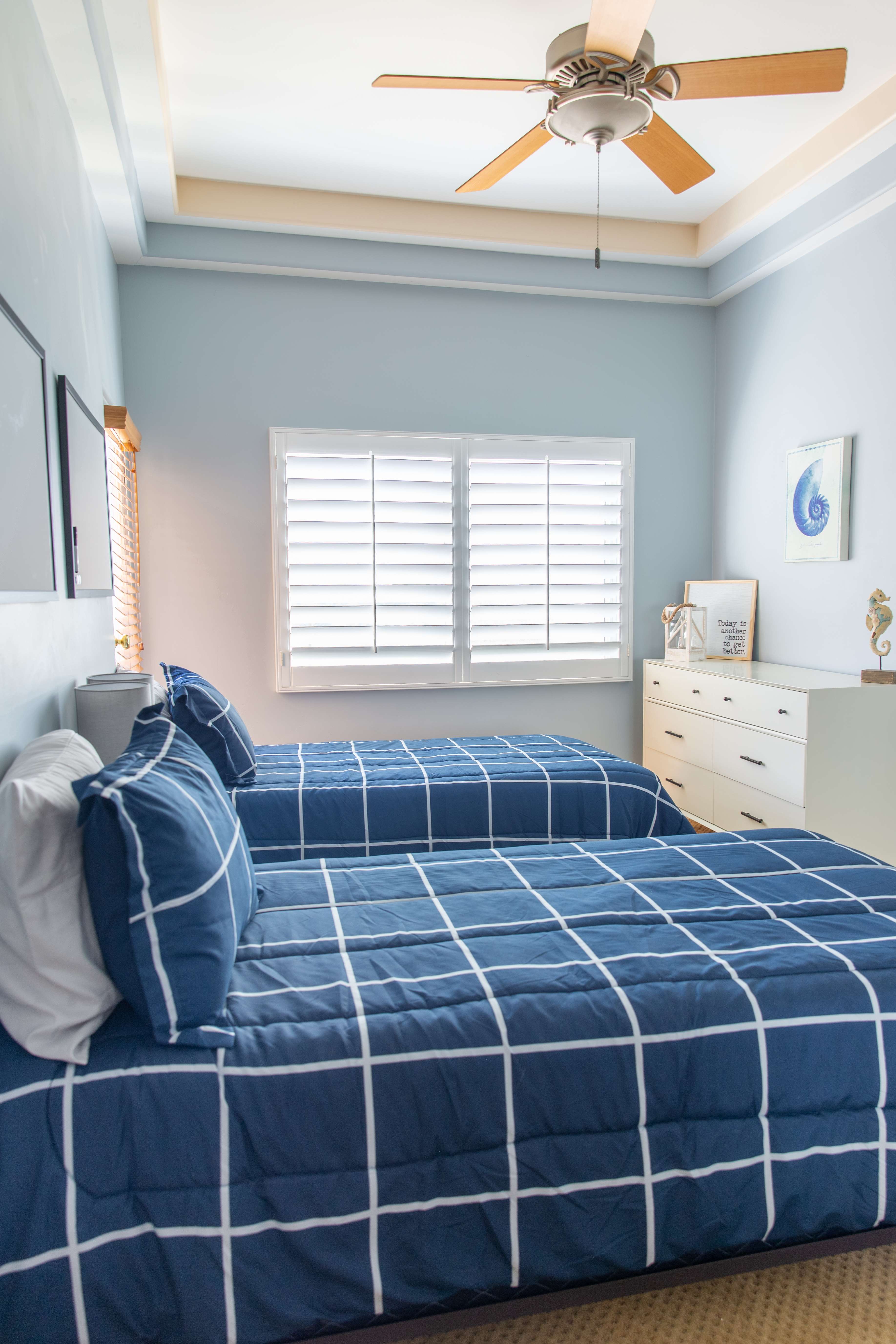 Room with two twin beds, ceiling fan, and window shutters