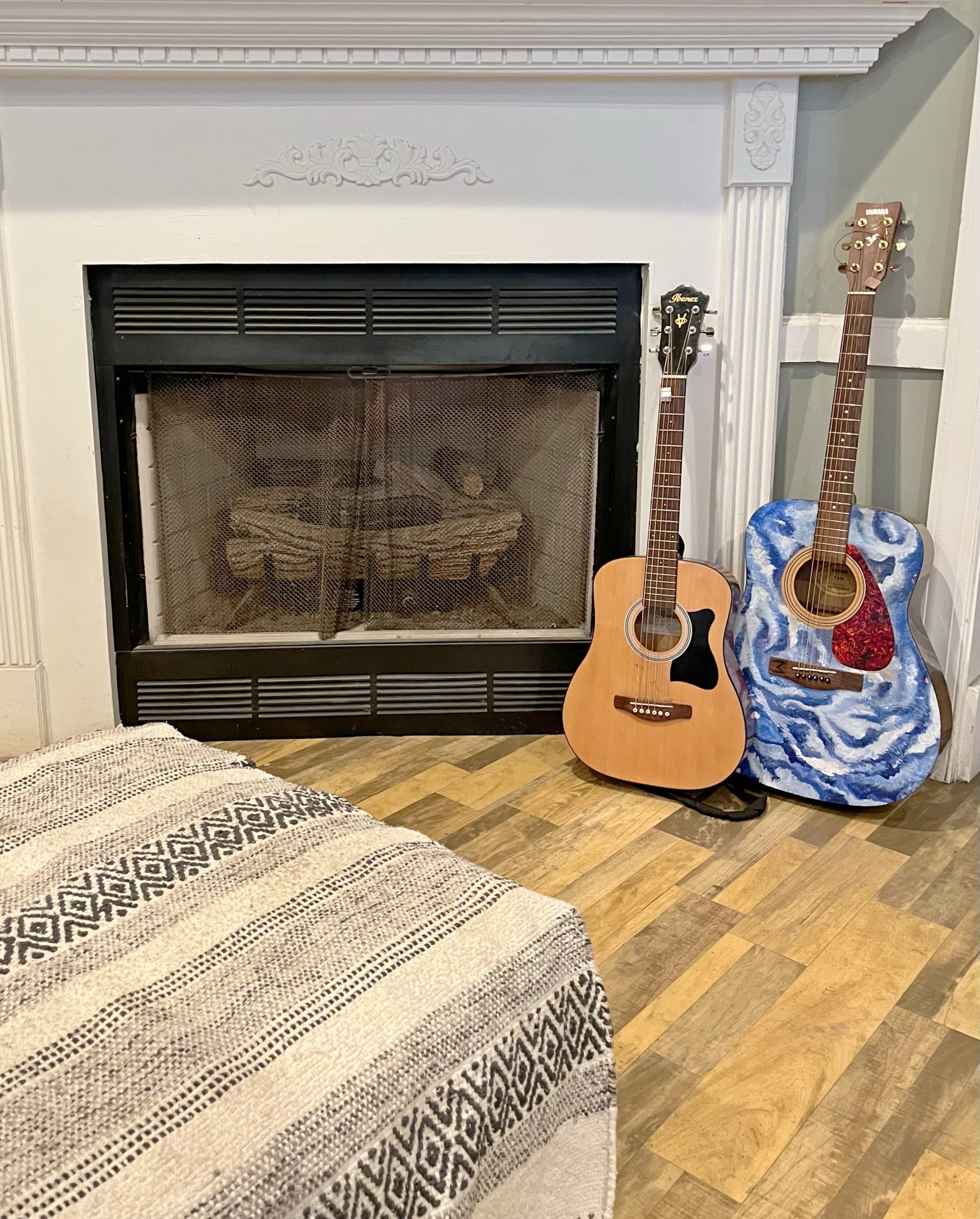 Two acoustic guitars beside a fireplace