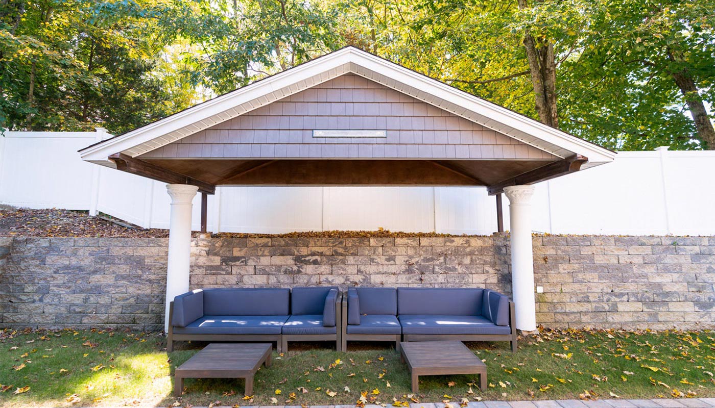 Covered outdoor lounge space with cushioned seating and trees.