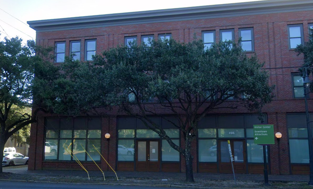 Three-story brick building with large trees and street sign