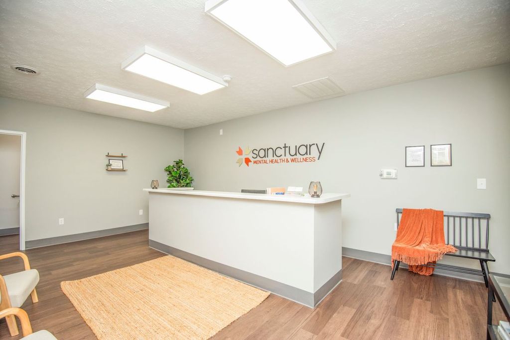 Reception area with white desk, bench, and Sanctuary logo on wall