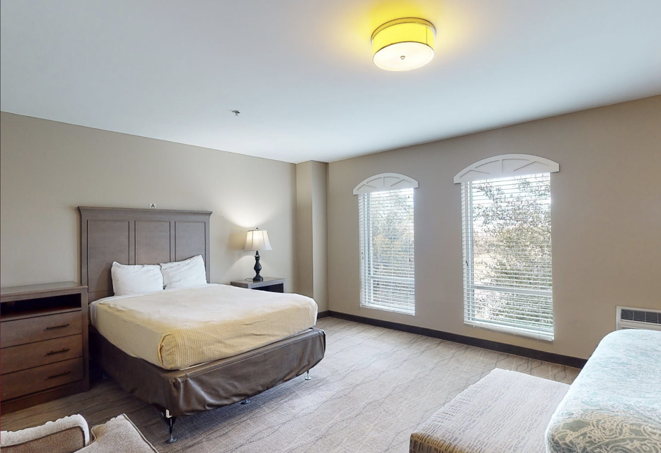 A spacious bedroom with a queen bed and large windows.