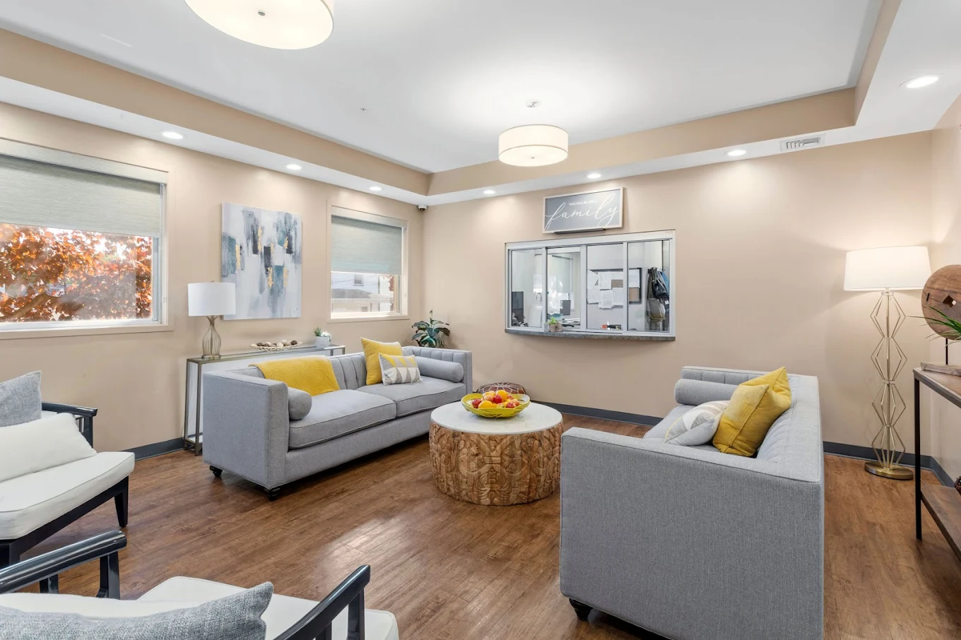 Bright seating area with gray couches, yellow pillows, and a windowed check-in counter